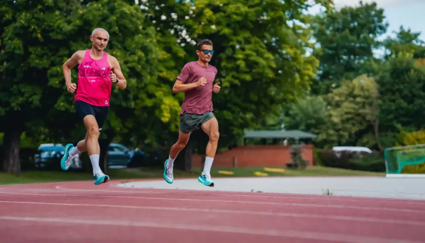 Dwóch biegaczy na bieżni, jeden w różowej koszulce, drugi w bordowej. Czas na 3 km!