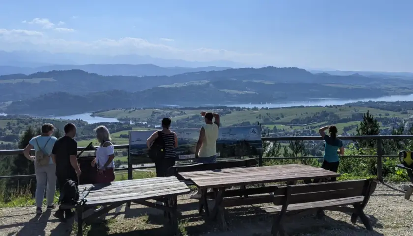 Grupa turystów podziwia rozległą panoramę z widokiem na jezioro i góry. Szlak na górę Wdżar oferuje takie widoki.