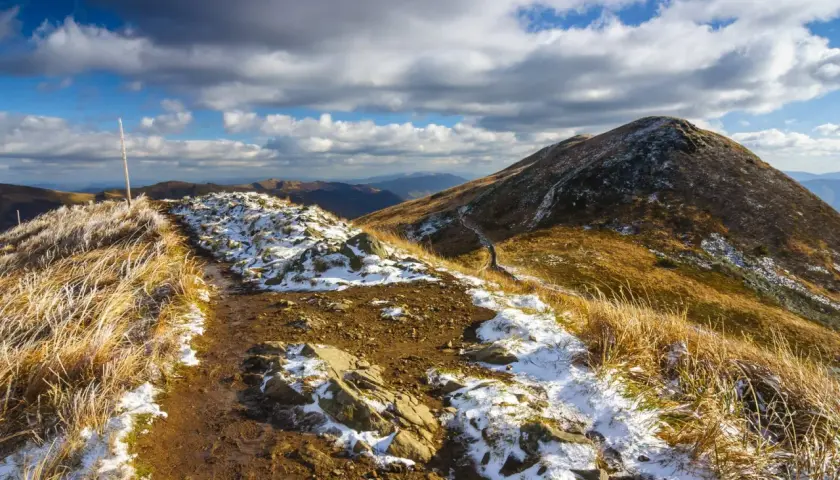 Szlak przez Bieszczady na Ukrainę, pokryty pierwszym śniegiem i jesienną trawą, pod burzowym niebem.