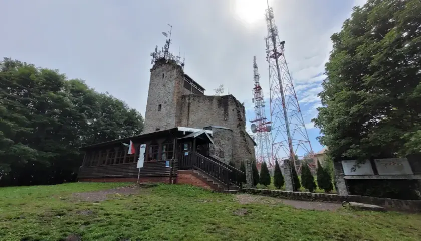Kamienna wieża i drewniana przybudówka na szczycie góry. W tle wysokie maszty telekomunikacyjne. To popularne miejsce na szlaki turystyczne, jak Chełmiec.