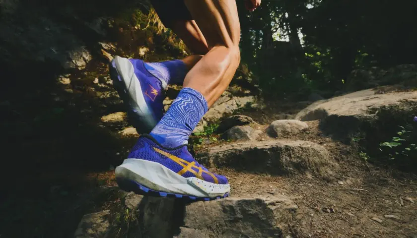 Czy buty do biegania nadają się do chodzenia? Zobacz, jak sportowiec pokonuje kamienisty szlak w fioletowych butach z żółtym logo.