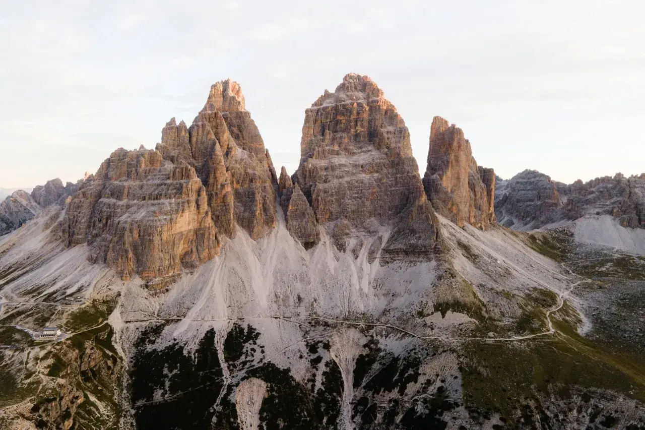 Majestatyczne **Tre Cime** w Dolomitach o wschodzie słońca. Skaliste szczyty i kręte ścieżki w otoczeniu surowego piękna.