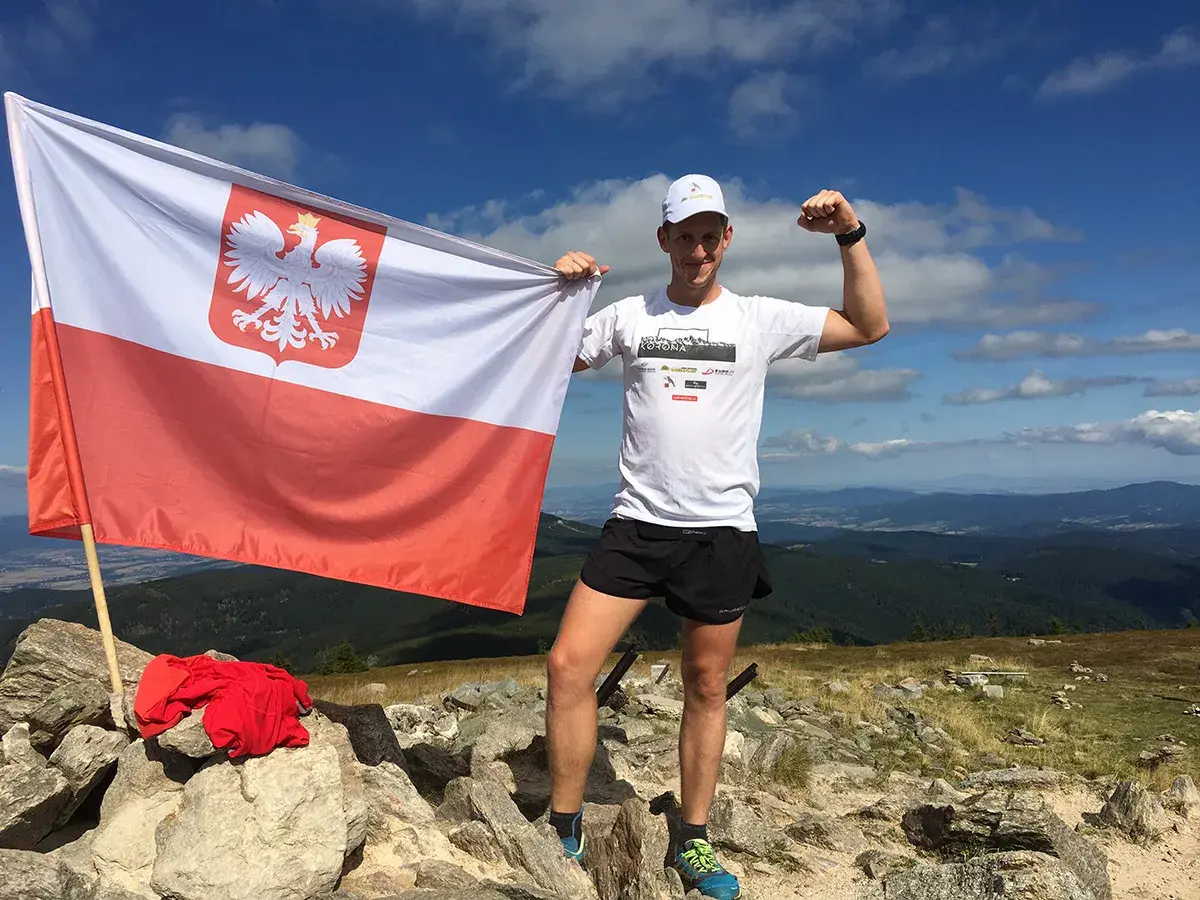 Mężczyzna na szczycie górskim z polską flagą, zdobywca diadem gór polskich.