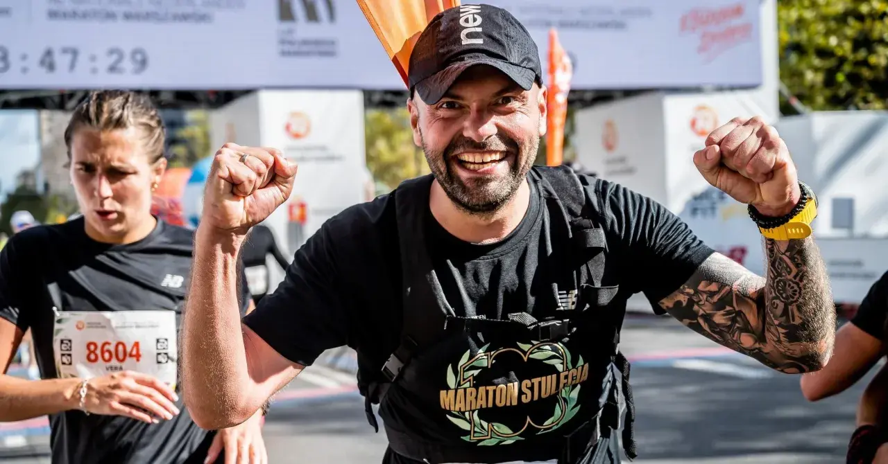 Piotr Łobodziński triumfuje na mecie maratonu, z dumą unosi pięści.