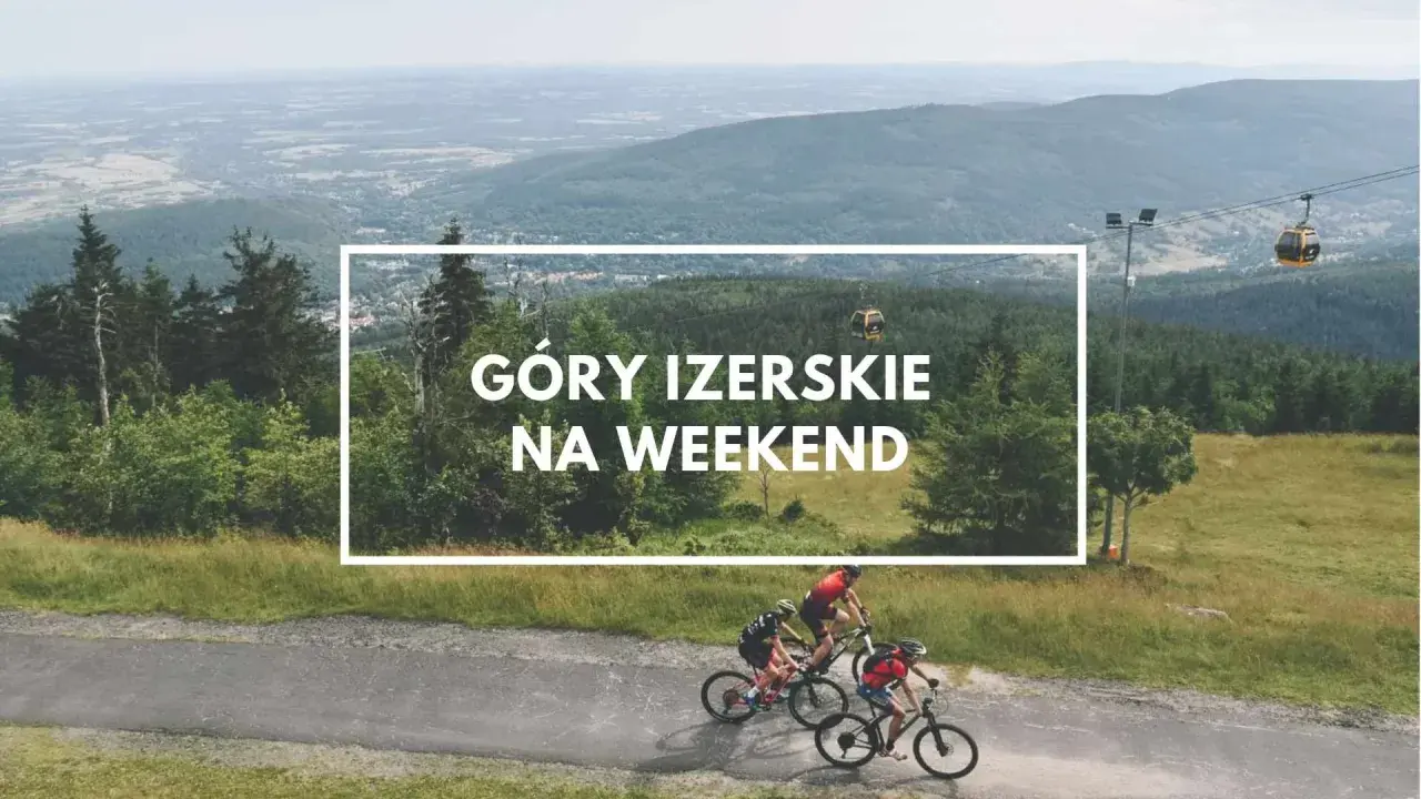 Trzech rowerzystów przemierza malownicze Góry Izerskie. W tle widać kolejkę gondolową i rozległą panoramę.