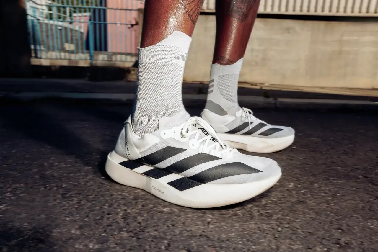 Biegacz w białych skarpetach i najdroższych butach do biegania z czarnymi paskami Adidas, gotowy na trening.