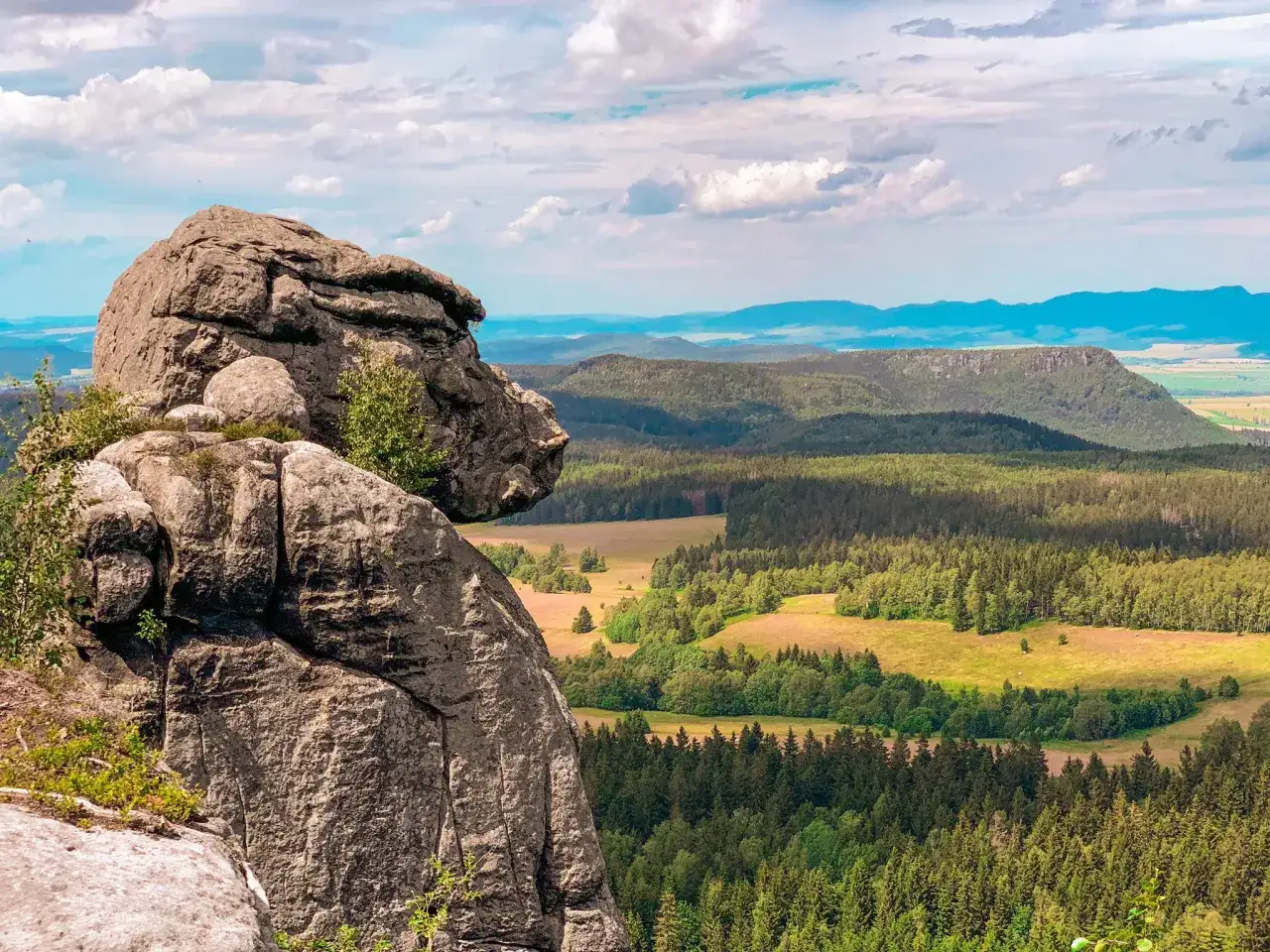 Skalny grzyb na szlaku w Górach Stołowych. Widok na zalesione doliny i pagórki w oddali.