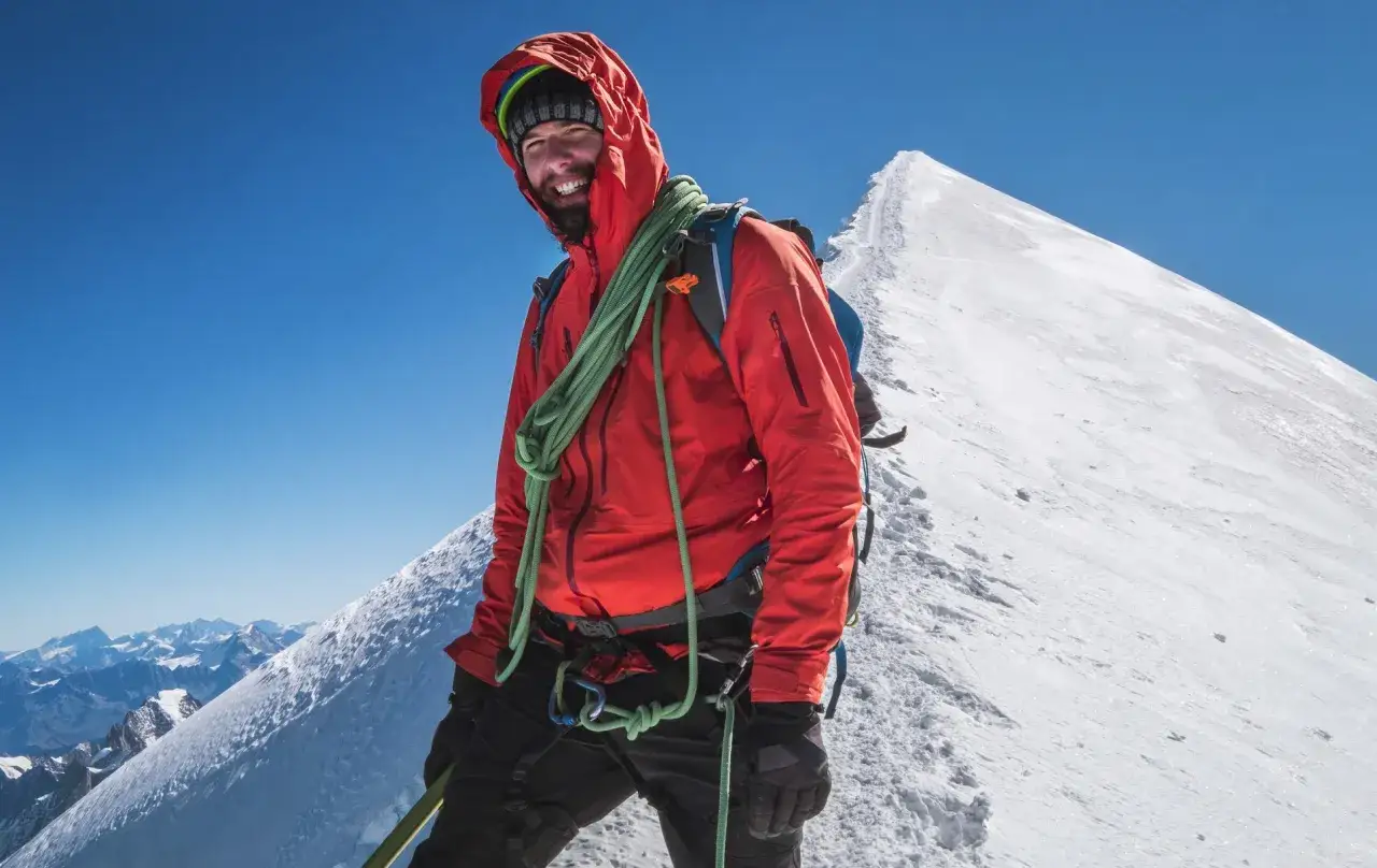 Szczęśliwy alpinista na szczycie, gotowy na wejście na Mont Blanc. W tle śnieżny grzbiet i błękitne niebo.