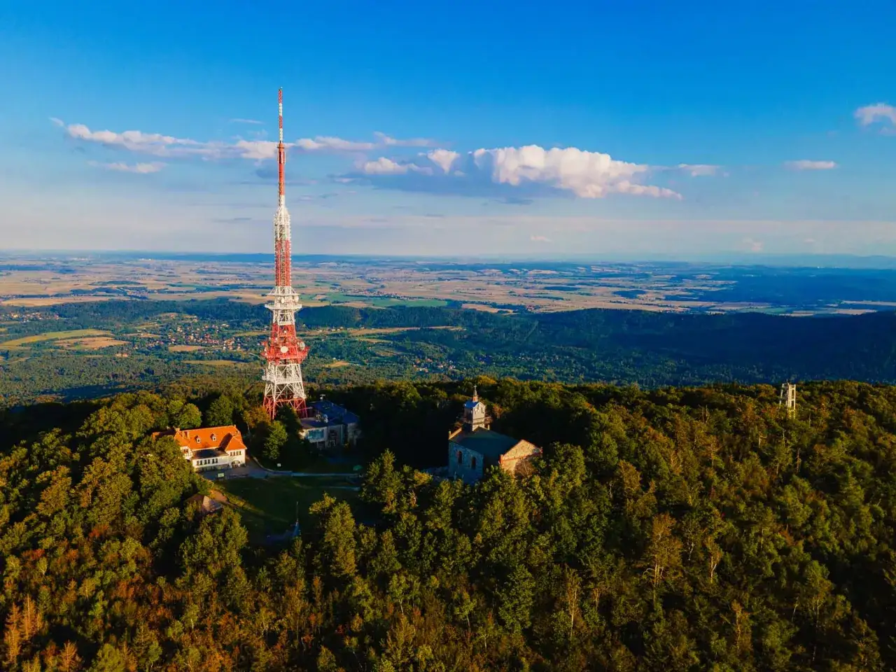 Wieża RTV na szczycie góry, otoczona lasem. Widać budynki i rozległą panoramę. Idealne miejsce na wędrówkę szlakami Ślęży.