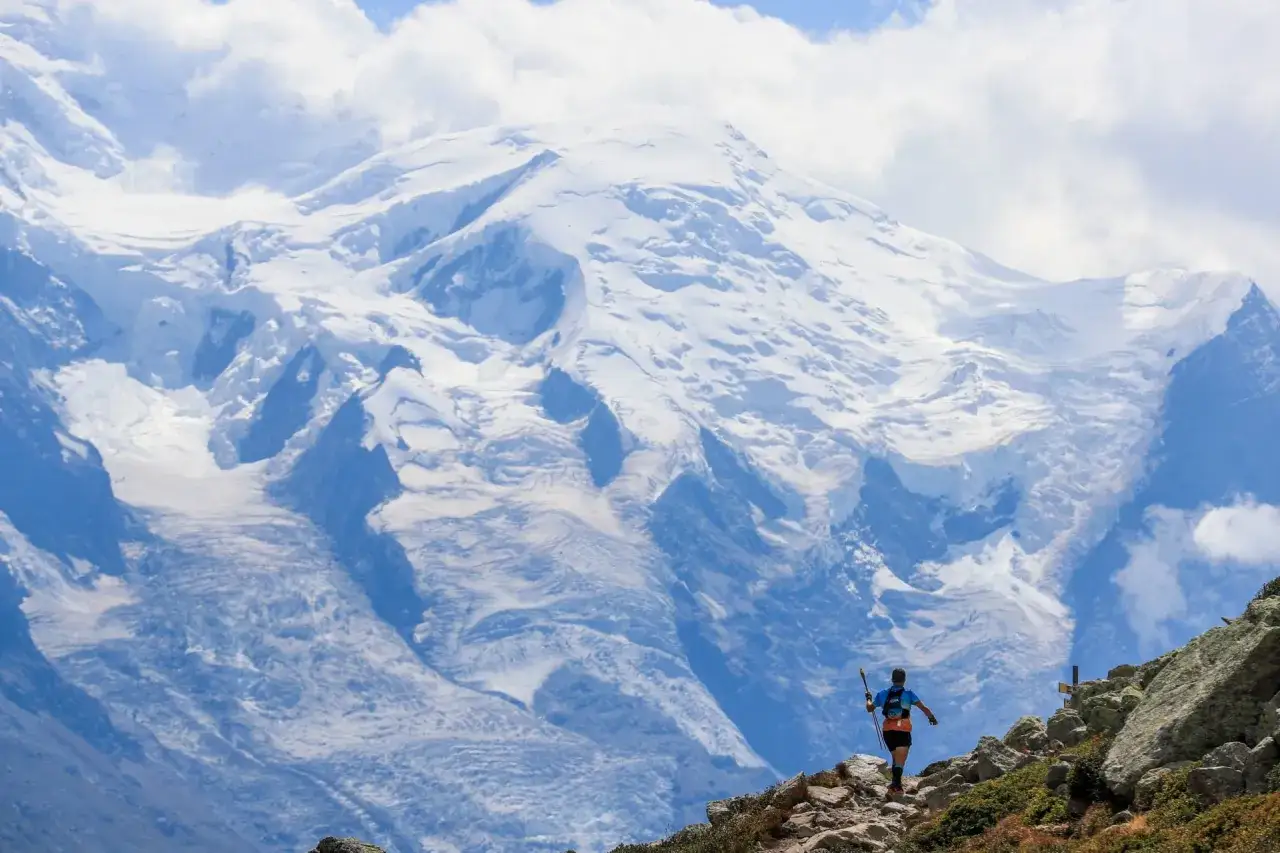 Biegacz na trasie ultra-trail du mont-blanc pokonuje kamienisty szlak na tle majestatycznych, ośnieżonych szczytów.