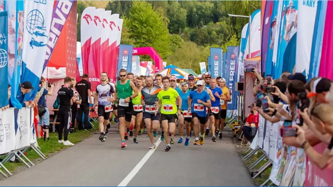 Uczestnicy festiwalu biegowego Piwniczna ruszają do startu wśród kolorowych flag i kibiców z aparatami.