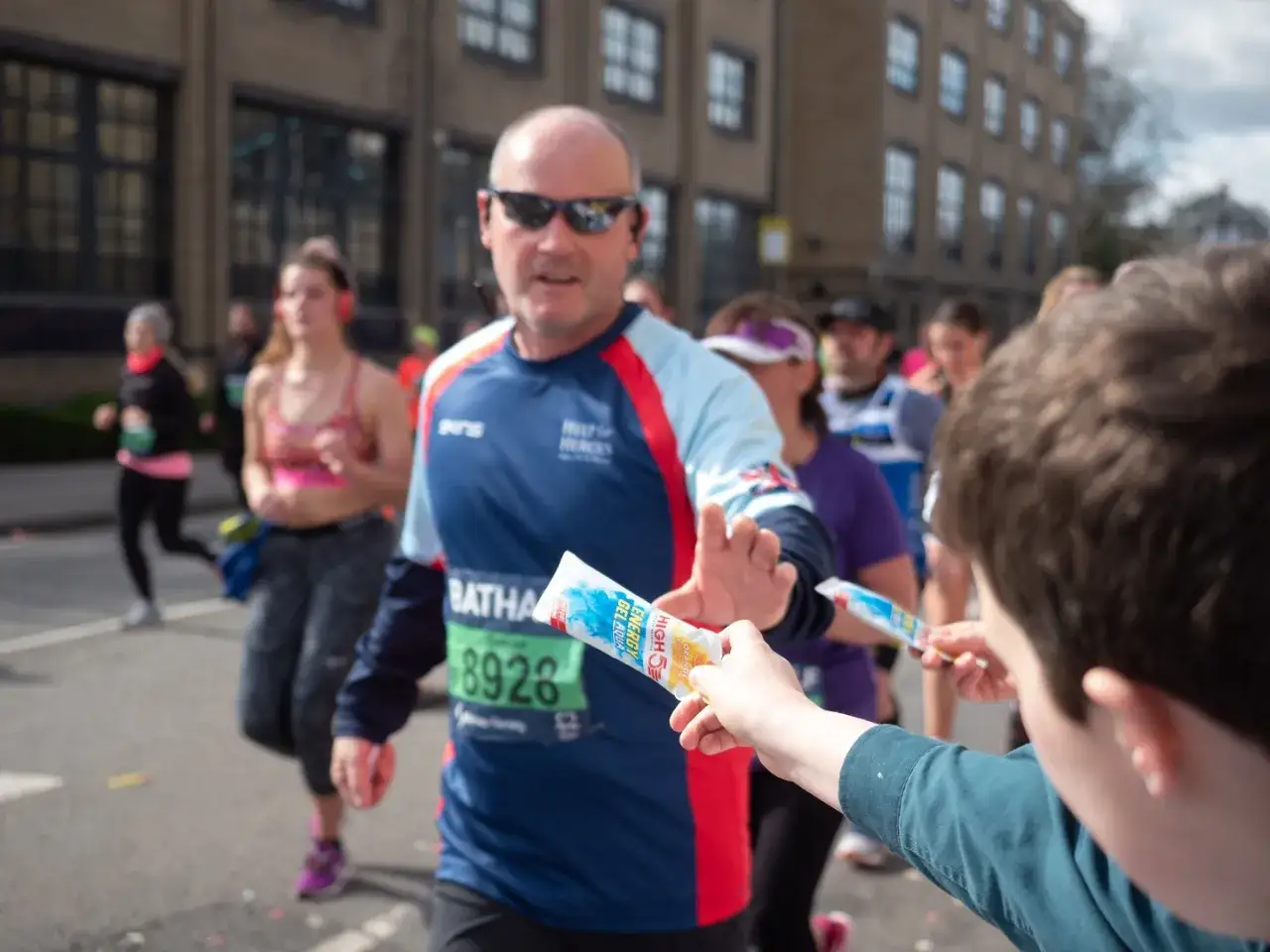 Chłopiec podaje biegaczowi żelki energetyczne podczas maratonu.
