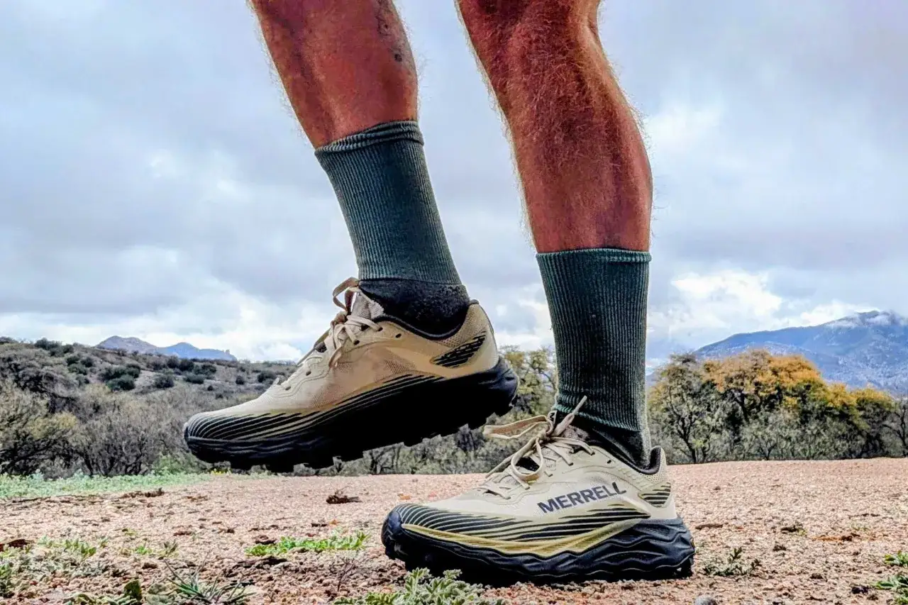 Beige buty trailowe Merrell z czarną podeszwą, gotowe na przygodę w g&oacute;rzystym terenie.